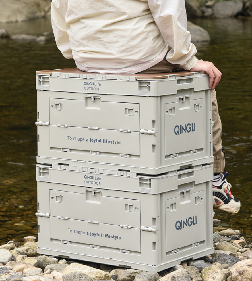 Person sitting on stacked Setstead 65L Multifunction Storage Boxes at a riverside campsite